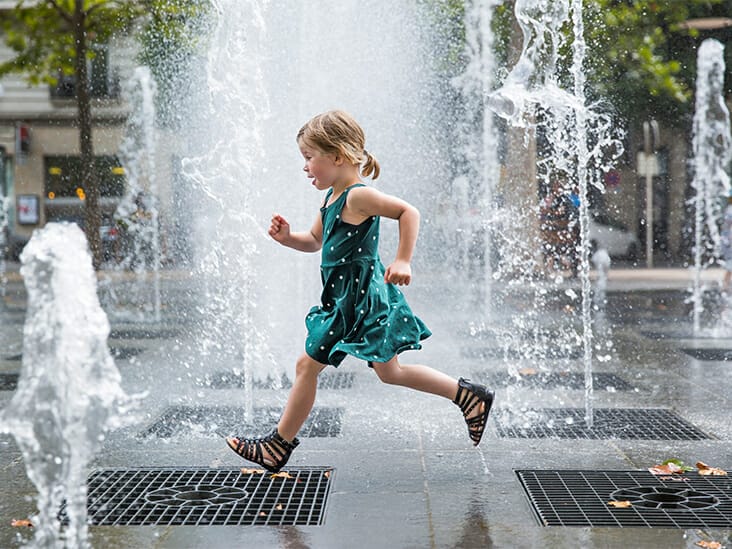 A girl is running in front of a fountain.