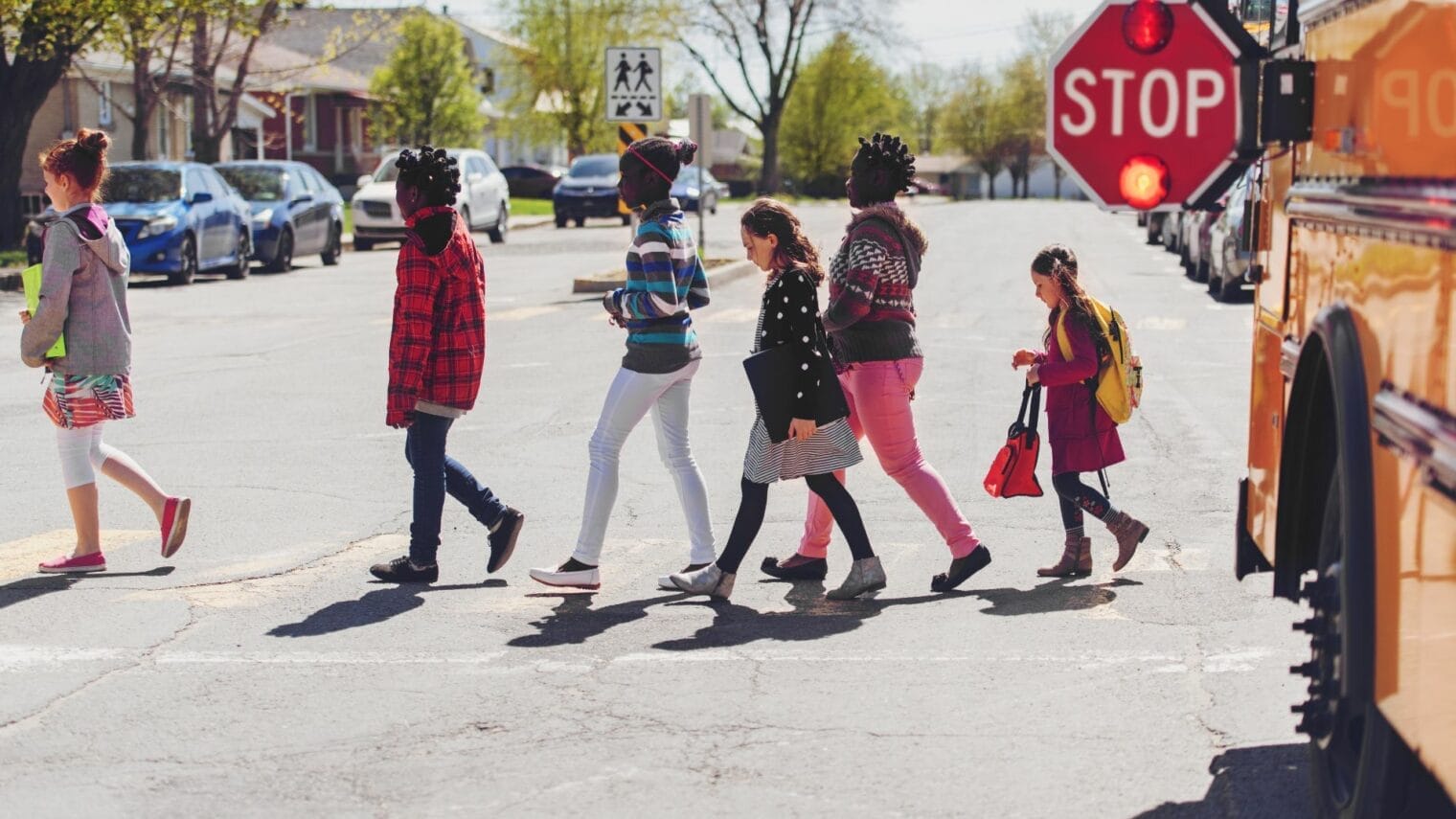 A group of children crossing the street in front of an auto draft school bus.