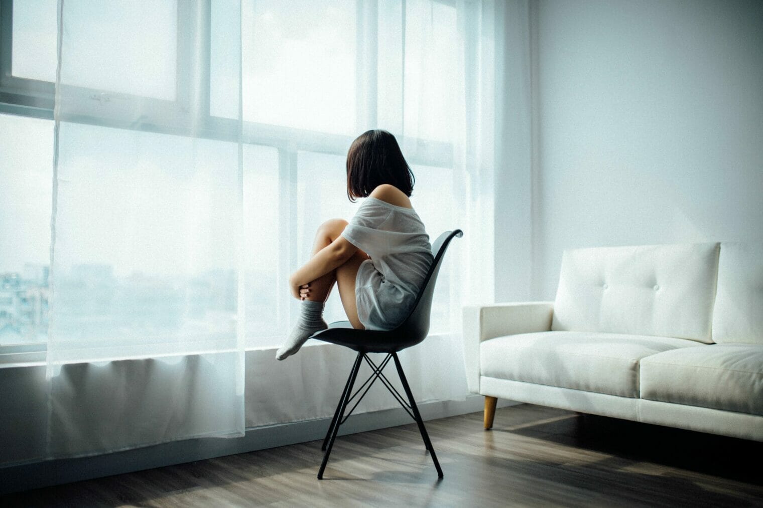 A woman sitting on a chair in front of a window, reflecting on the pressing workforce shortage and the need for improved mental healthcare.