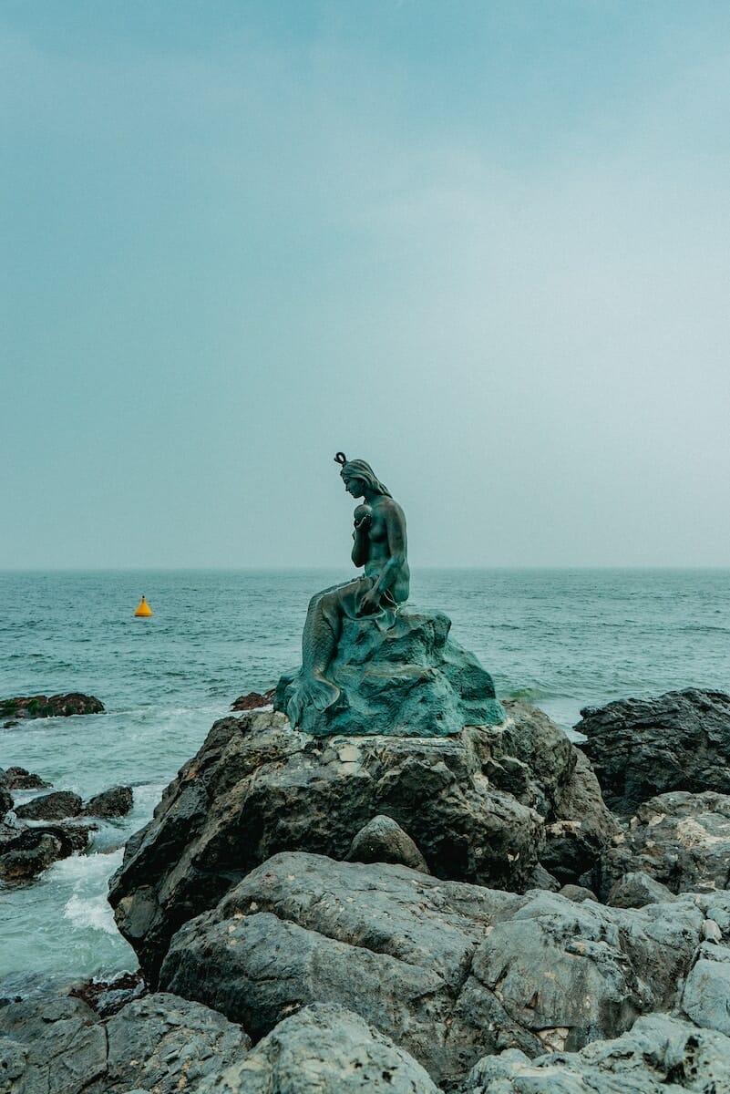 The little mermaid statue on the rocks by the ocean promotes youth wellness.